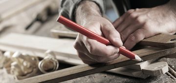 man marking piece of wood to carve